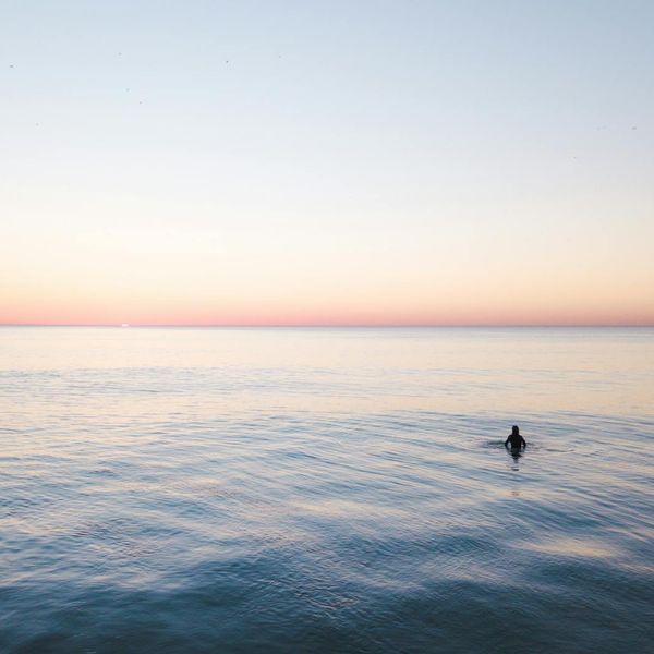Person meditating peacefully outdoors during sunset with soft pink sky.